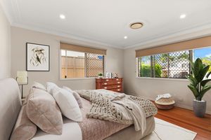 Styled master bedroom with layered bedding, timber floors, crown molding, decorative art, and dual windows.