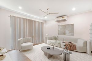 Elegant white living room with curved sofa, round coffee table, ceiling fan, and split system air conditioner.