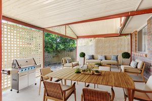 Stylish alfresco entertaining area with timber dining set, outdoor sofa, BBQ, and lattice privacy screen.