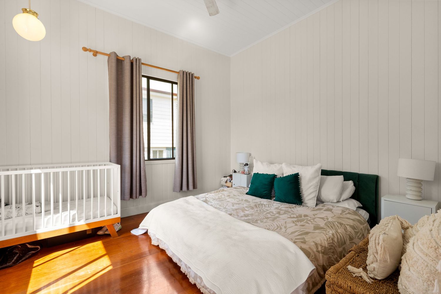 Cozy bedroom with white crib, queen bed with teal cushions, timber floors, and shiplap wall paneling.