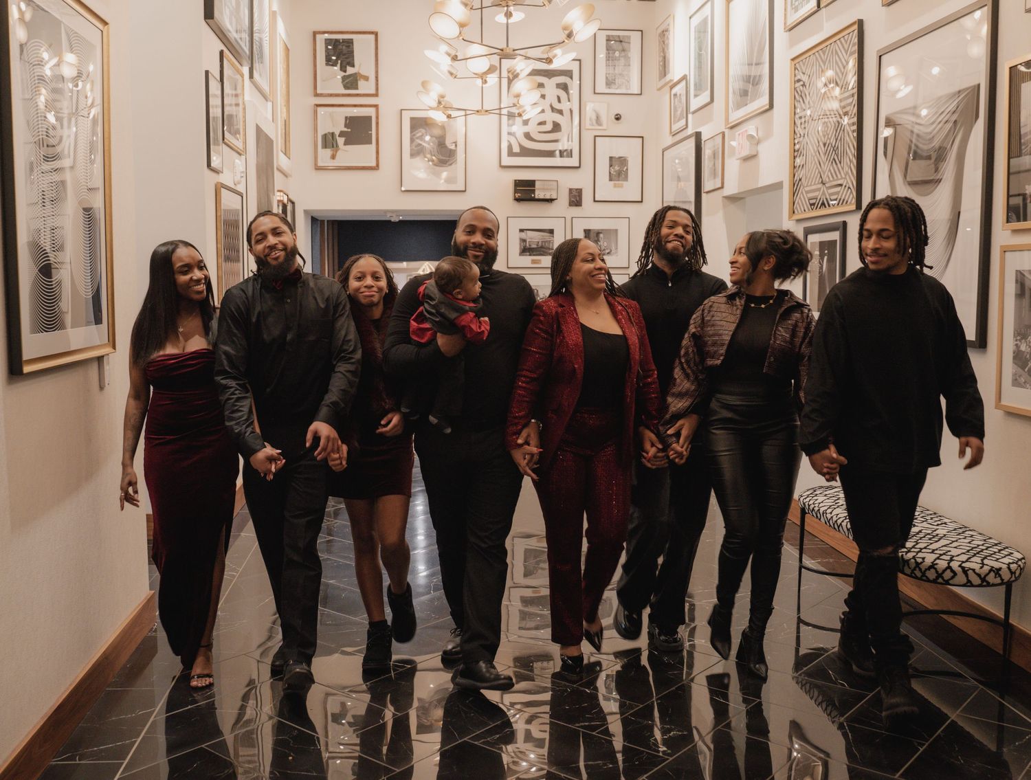 A group of people walk through an art gallery hallway with framed artwork displayed on white walls.