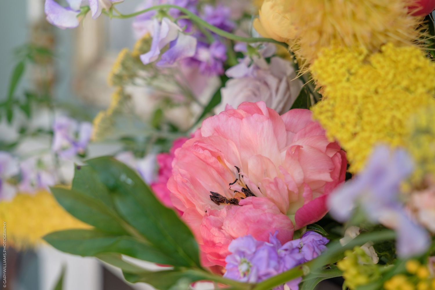 Colorful spring flower bouquet featuring pink peonies, yellow mimosa, and purple blooms in a soft, dreamy arrangement.