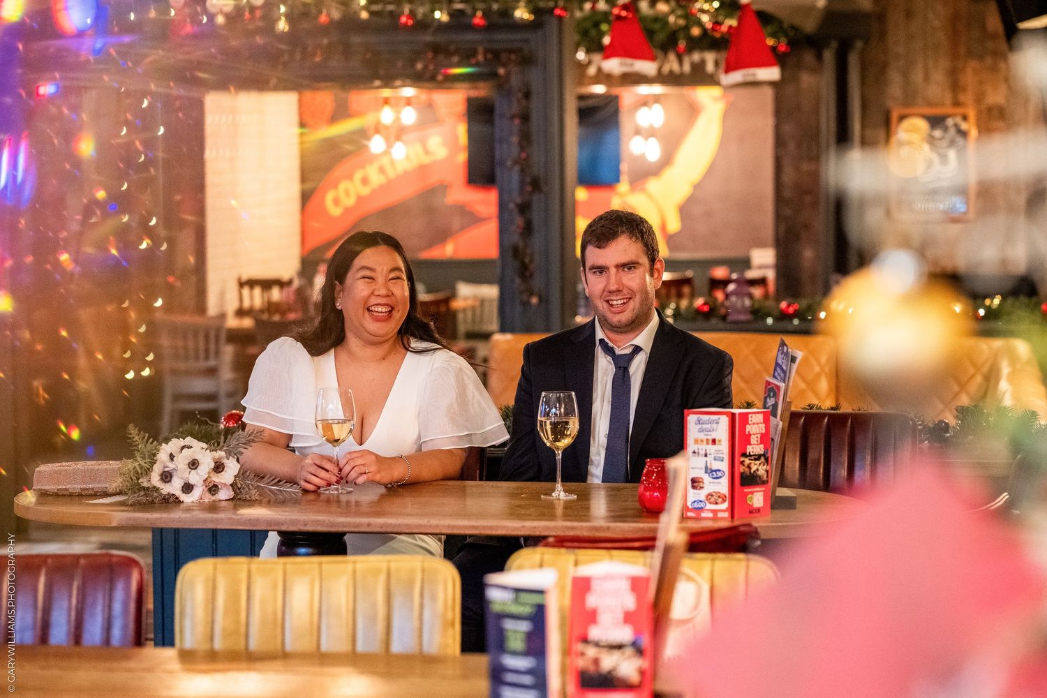Two people sitting at a bar counter in a festively decorated holiday setting.