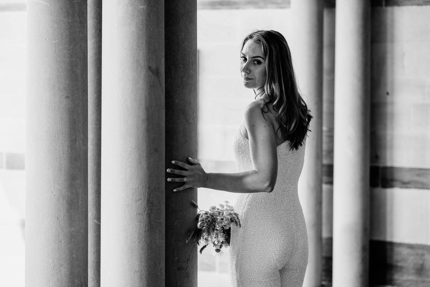 A woman stands topless, facing away from the camera, in a black and white photograph.