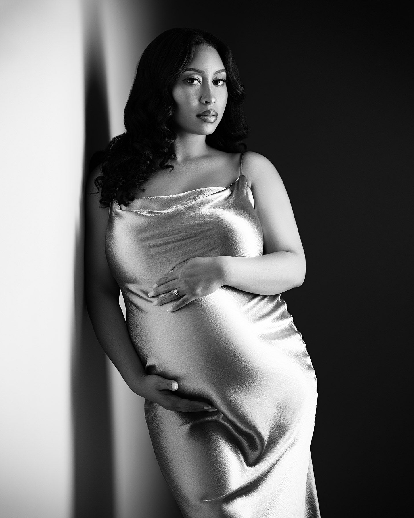 A black and white portrait of a woman wearing a satin dress, posing with her arms crossed.