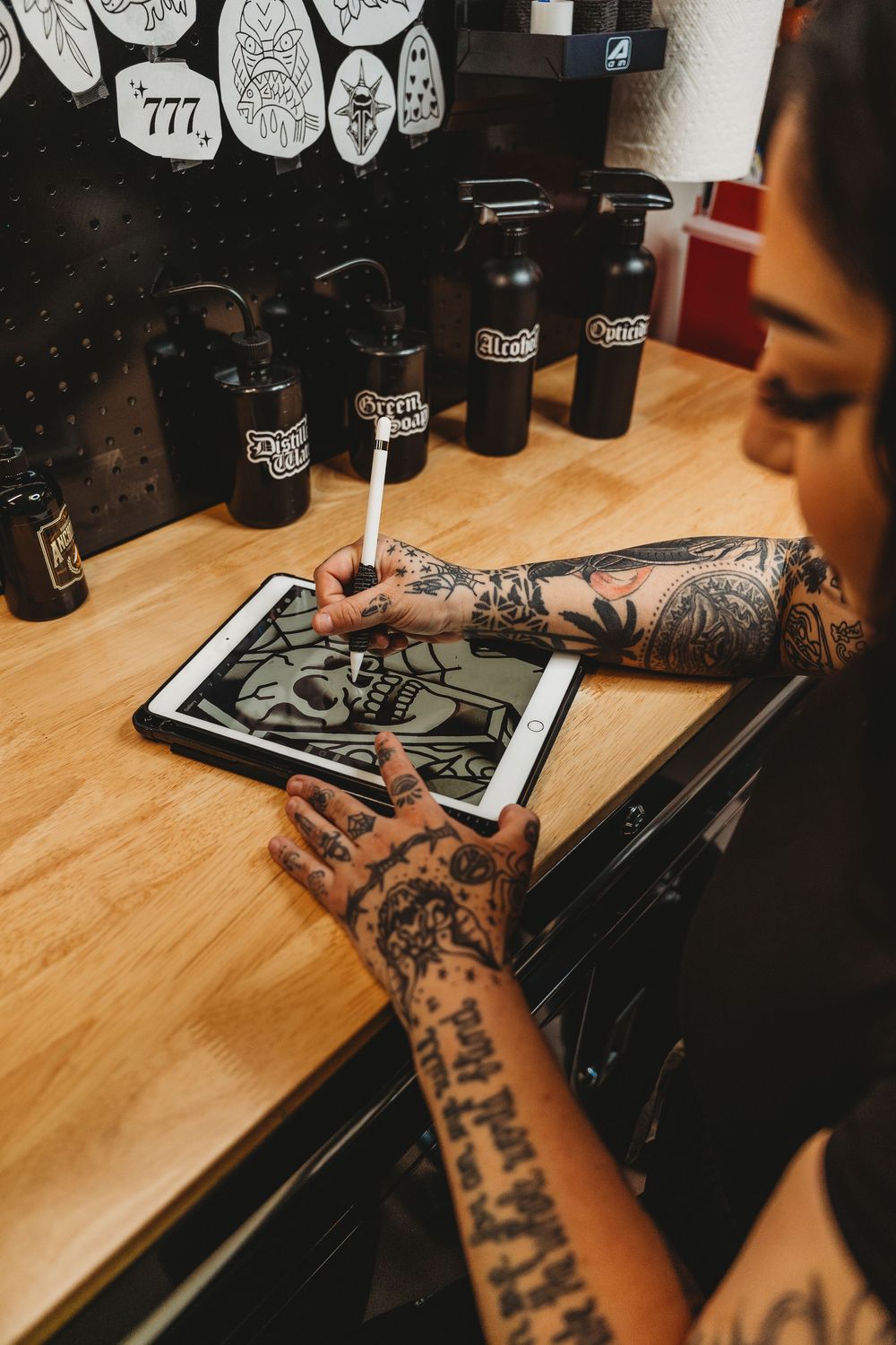 Heavily tattooed woman drawing skull design on digital tablet in tattoo studio workspace. Tattoo artist branding photos. Jacksonville, NC