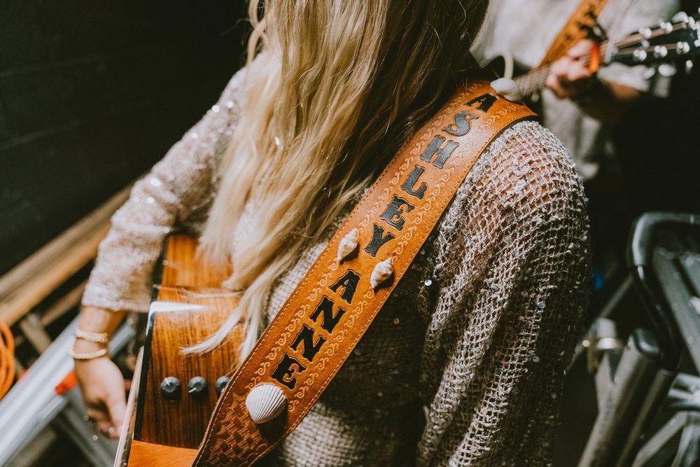 Close-up of woman playing guitar with custom leather strap in rustic performance setting. Live music photography Jacksonville NC