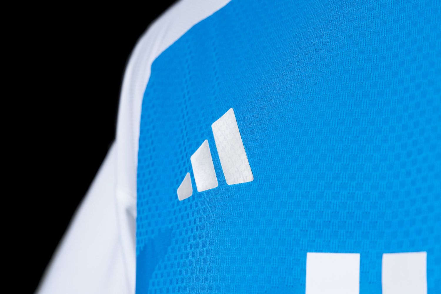 Close-up of white Adidas logo on blue and white Charlotte FC soccer jersey.
