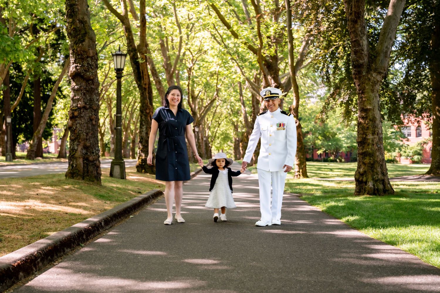 Romantic couple walking through tree-lined path in outdoor summer setting.