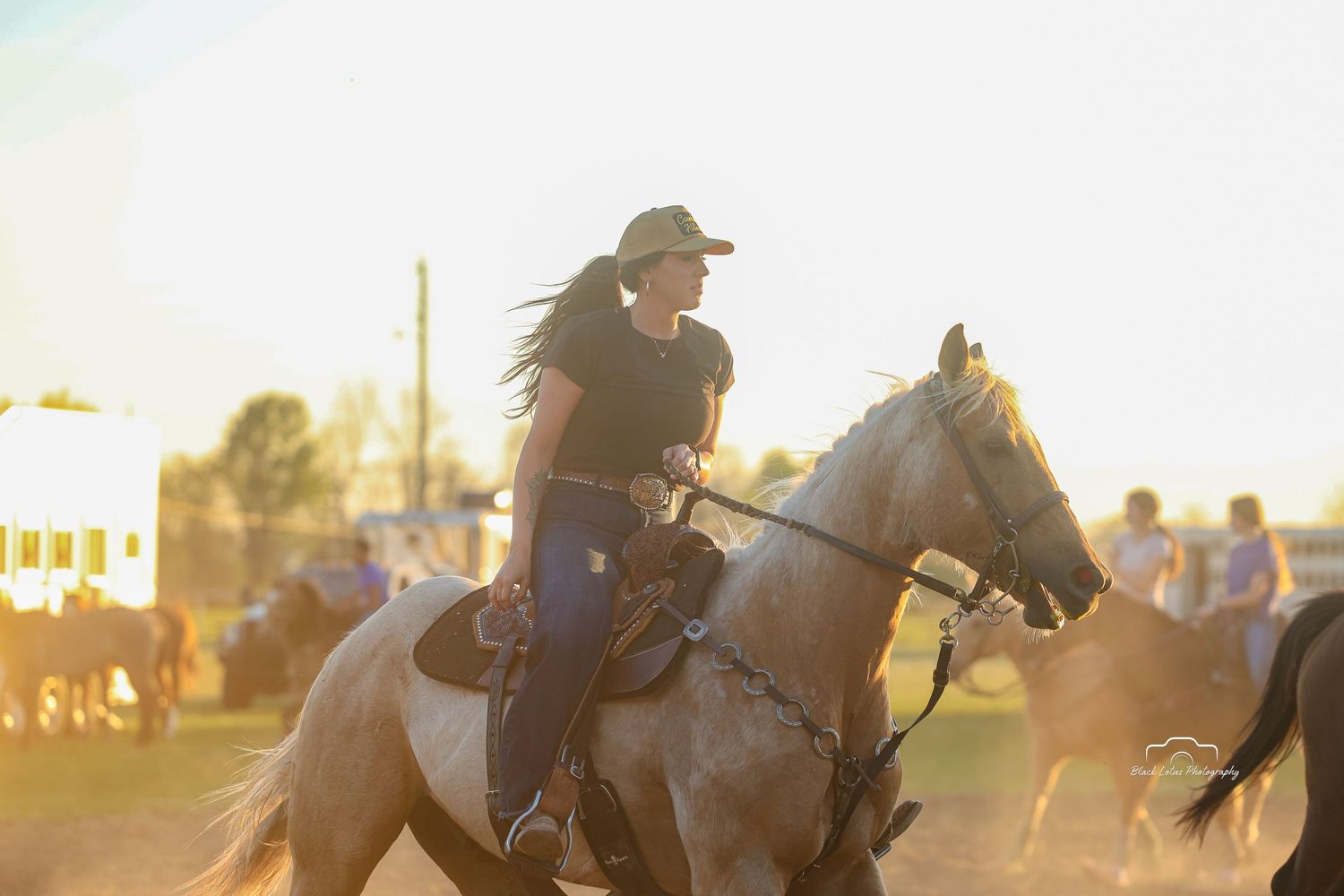 Woman riding a palomino horse at golden hour during an outdoor equestrian event.