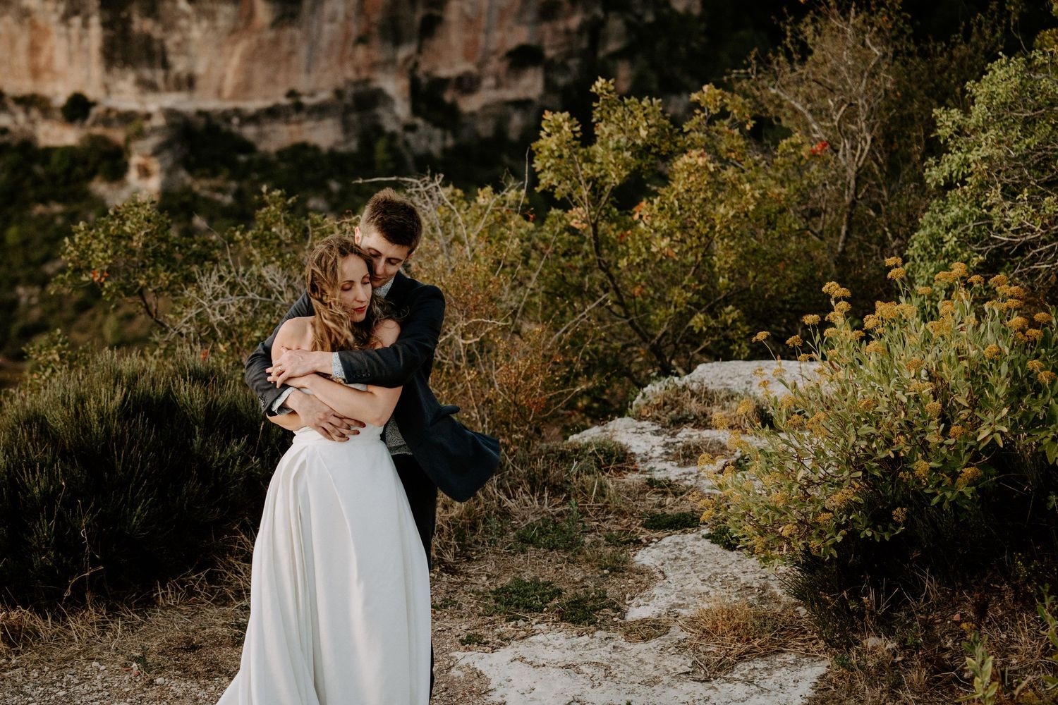 Couple embracing on rocky mountain trail surrounded by autumn foliage and cliffs.