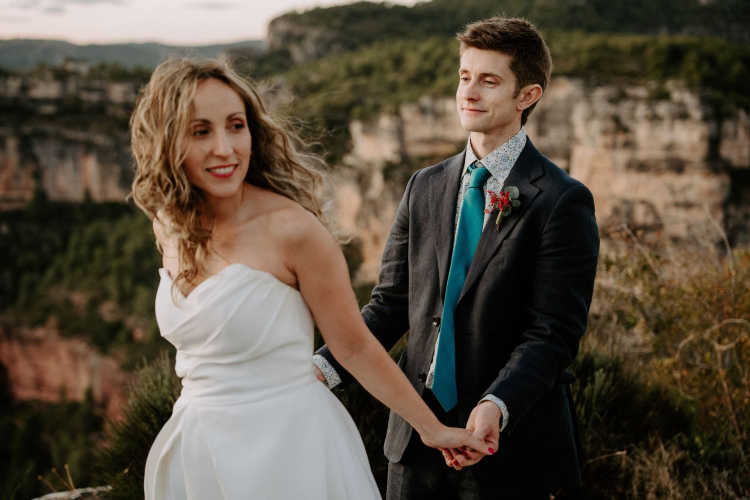 Newlyweds share intimate moments on a scenic cliff edge during sunset.