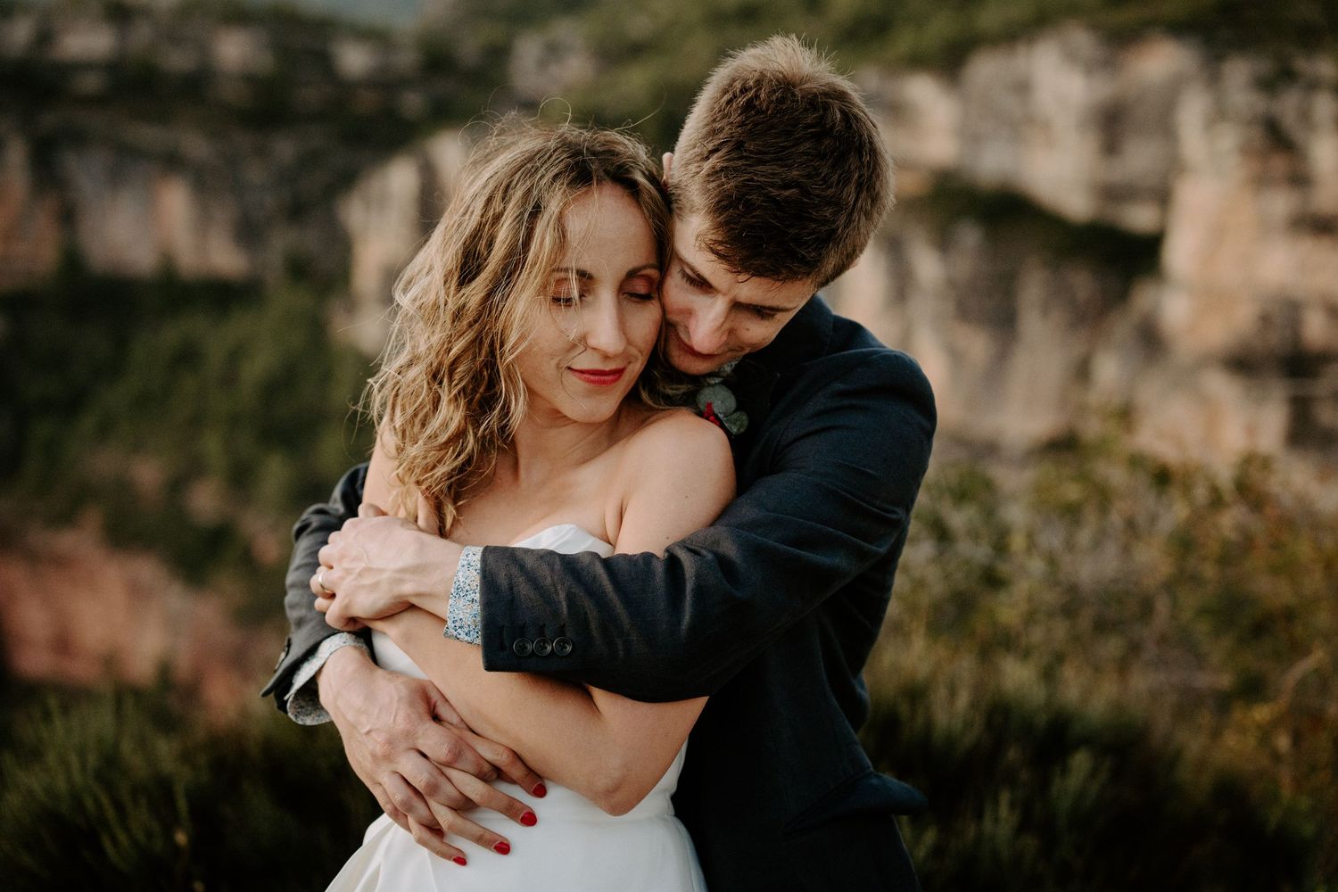 Intimate embrace captured against rugged mountain cliffs at golden hour.