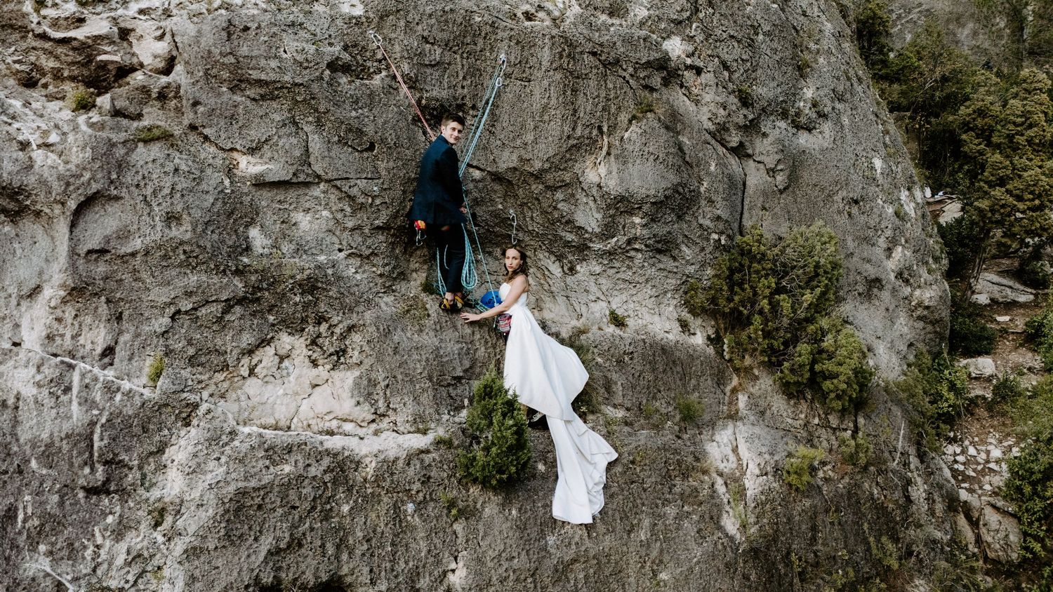 A person in white clothing climbs a steep rock face using climbing gear and safety equipment.