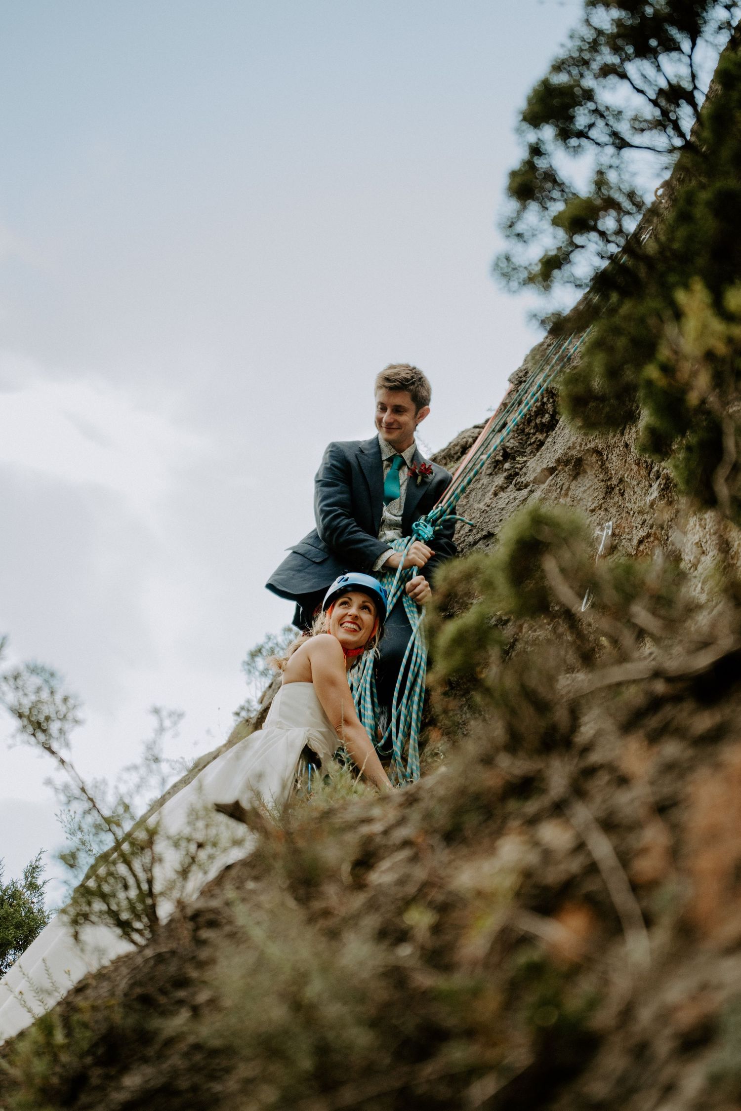 A couple in formal attire poses dramatically on a rocky cliff edge during their adventure session.