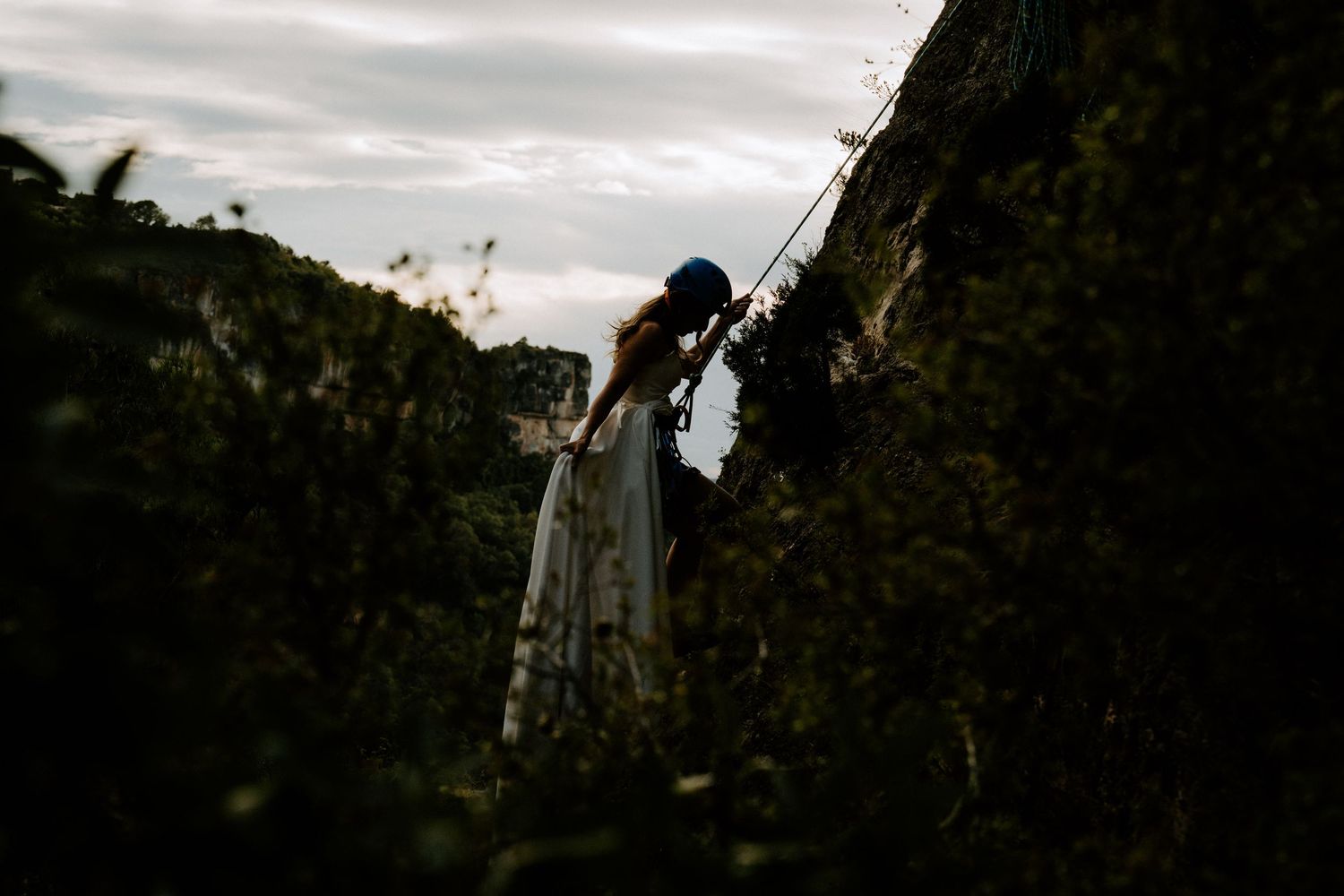 A silhouetted figure in a flowing white dress stands against a moody sky near a tree at dusk.