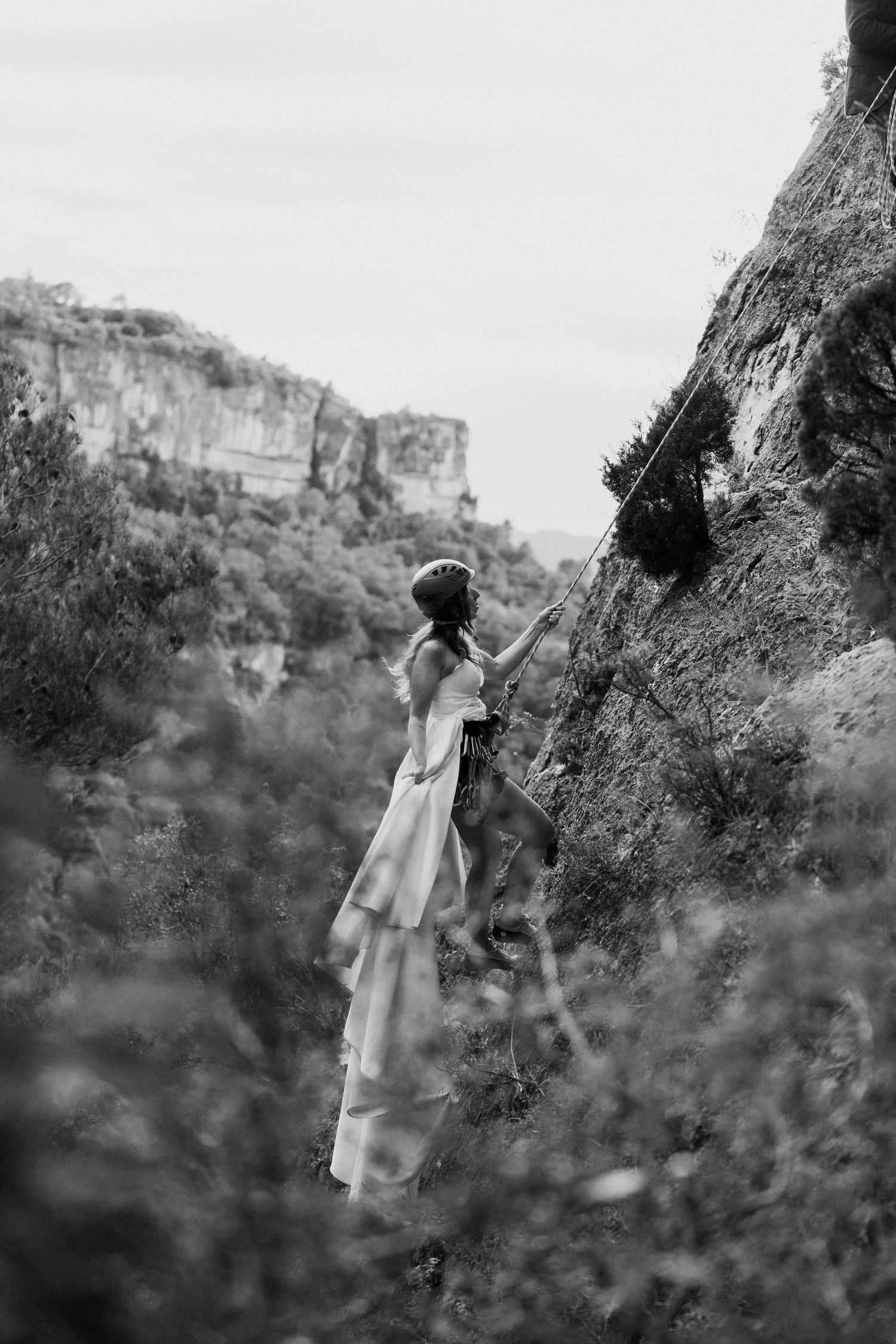 A figure in a flowing white dress climbing a steep rock face in black and white.