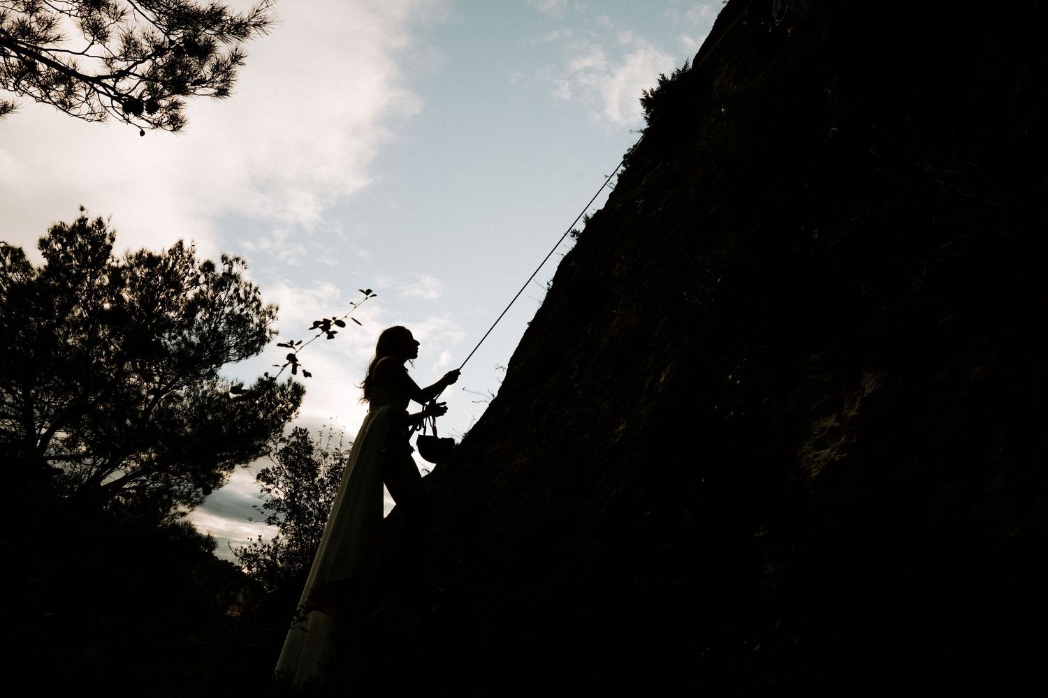 Silhouetted figures stand against a dramatic sunset sky with trees framing the scene.
