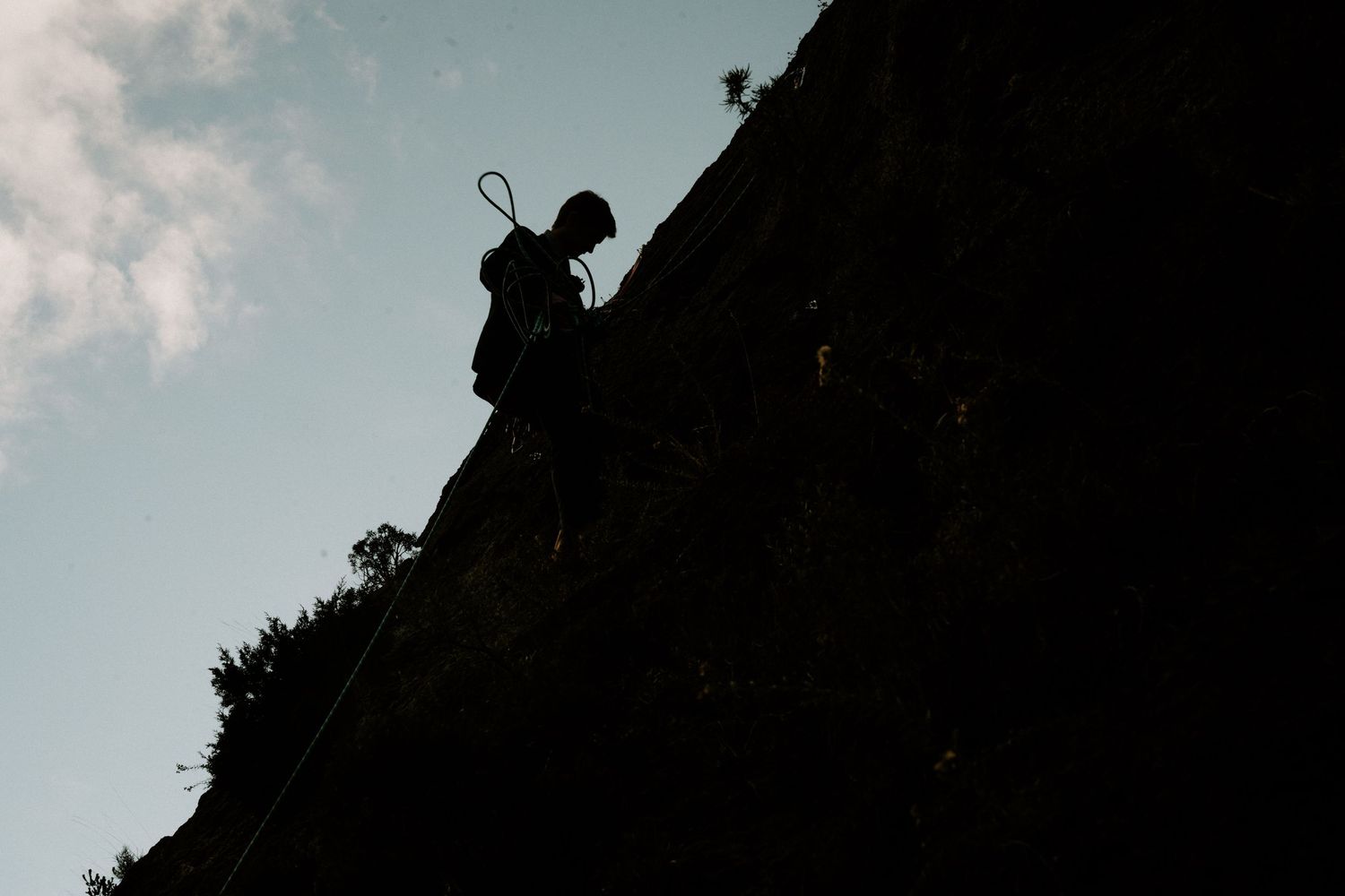 Silhouette of a rock climber scaling a steep cliff face against a cloudy sky.