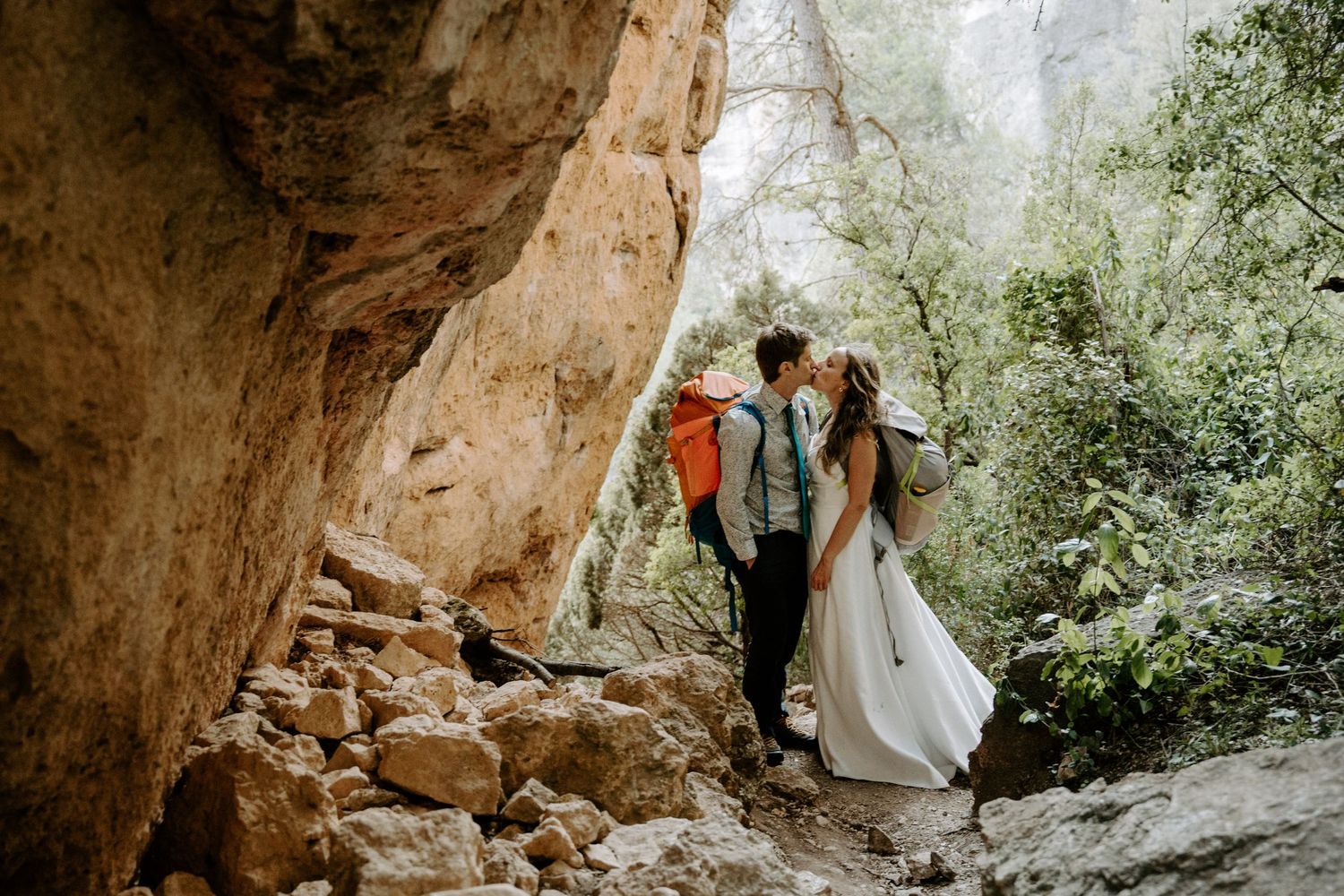 A couple in wedding attire explores a dramatic cave formation during their adventure session.