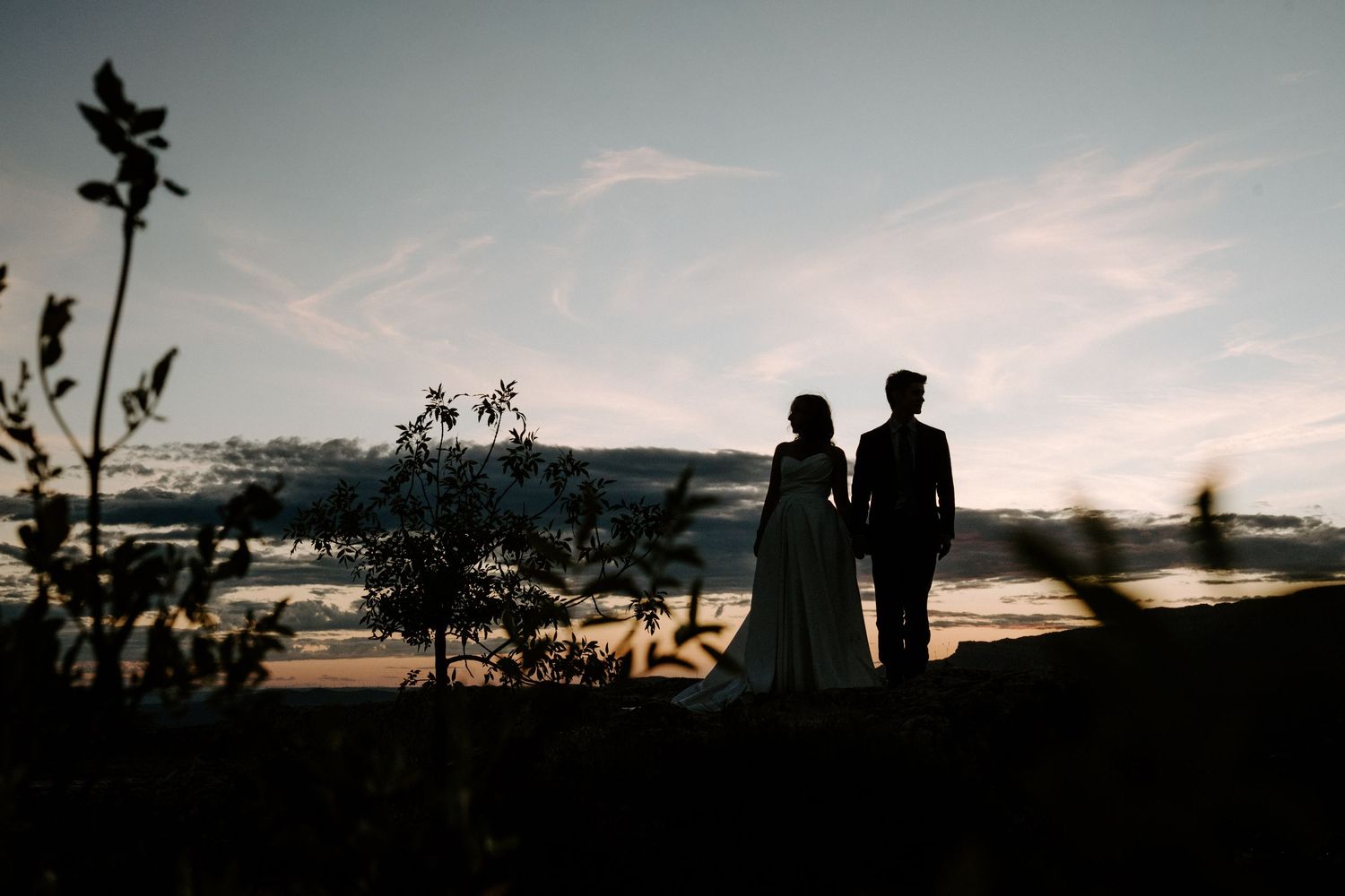 Silhouetted couple stands together against a sunset beach backdrop with palm trees in Hawaii.