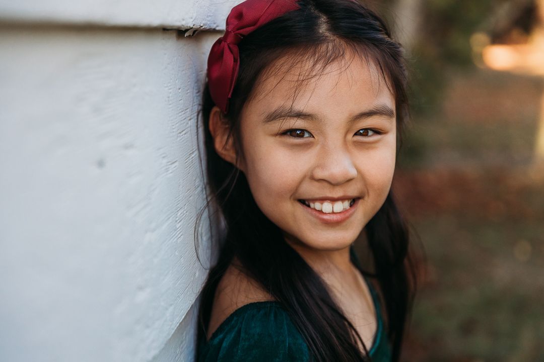 A person with long dark hair smiles warmly while sitting outdoors during golden hour lighting.