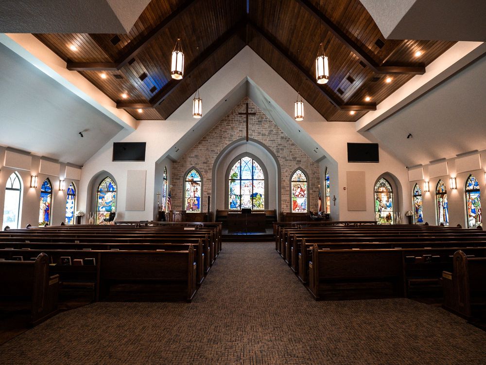 Interior view of a traditional church sanctuary with wooden pews, stained glass windows, and vaulted ceilings.