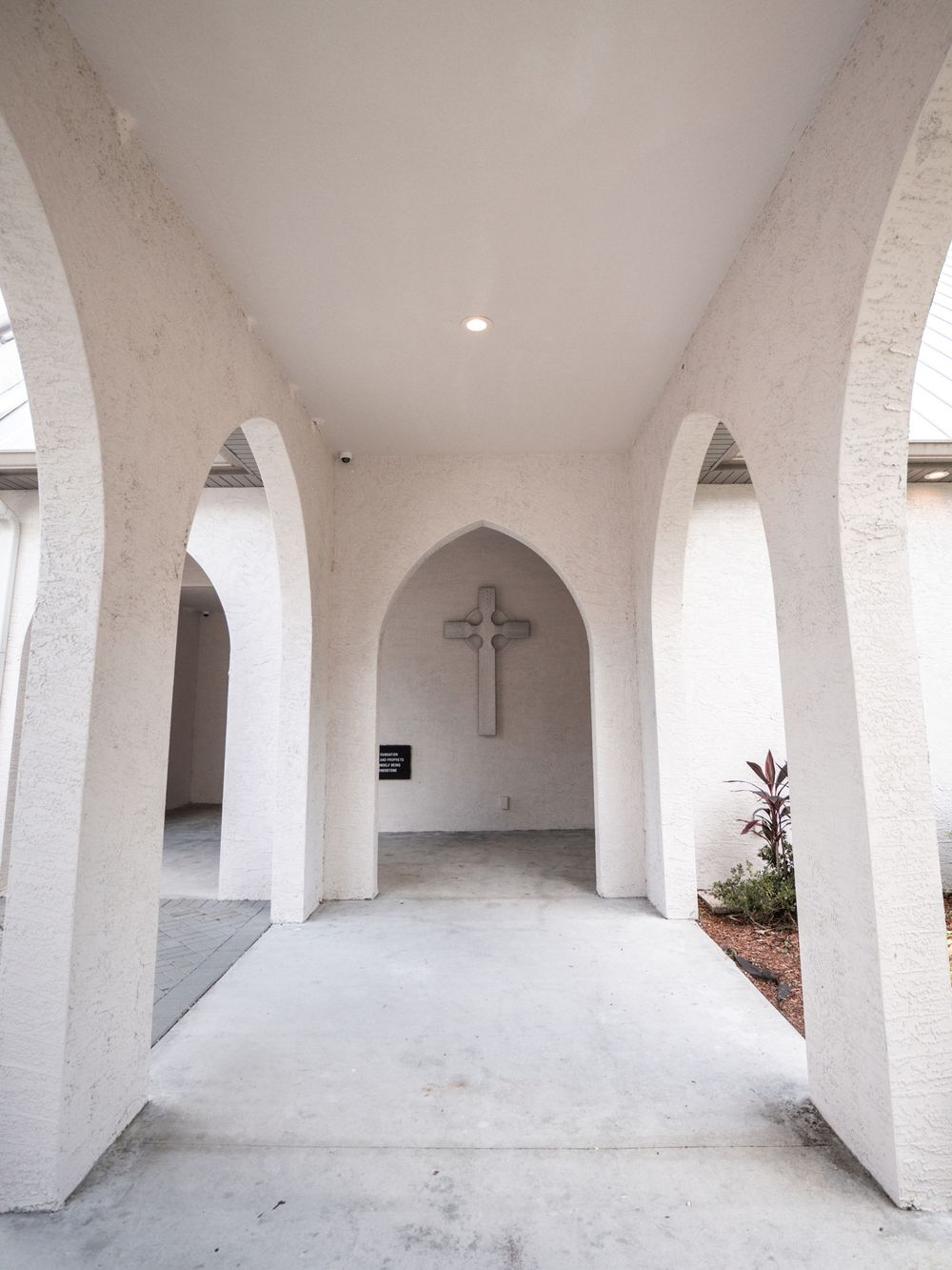 White arched hallway in a church with a crucifix mounted on the wall at the end of the corridor.