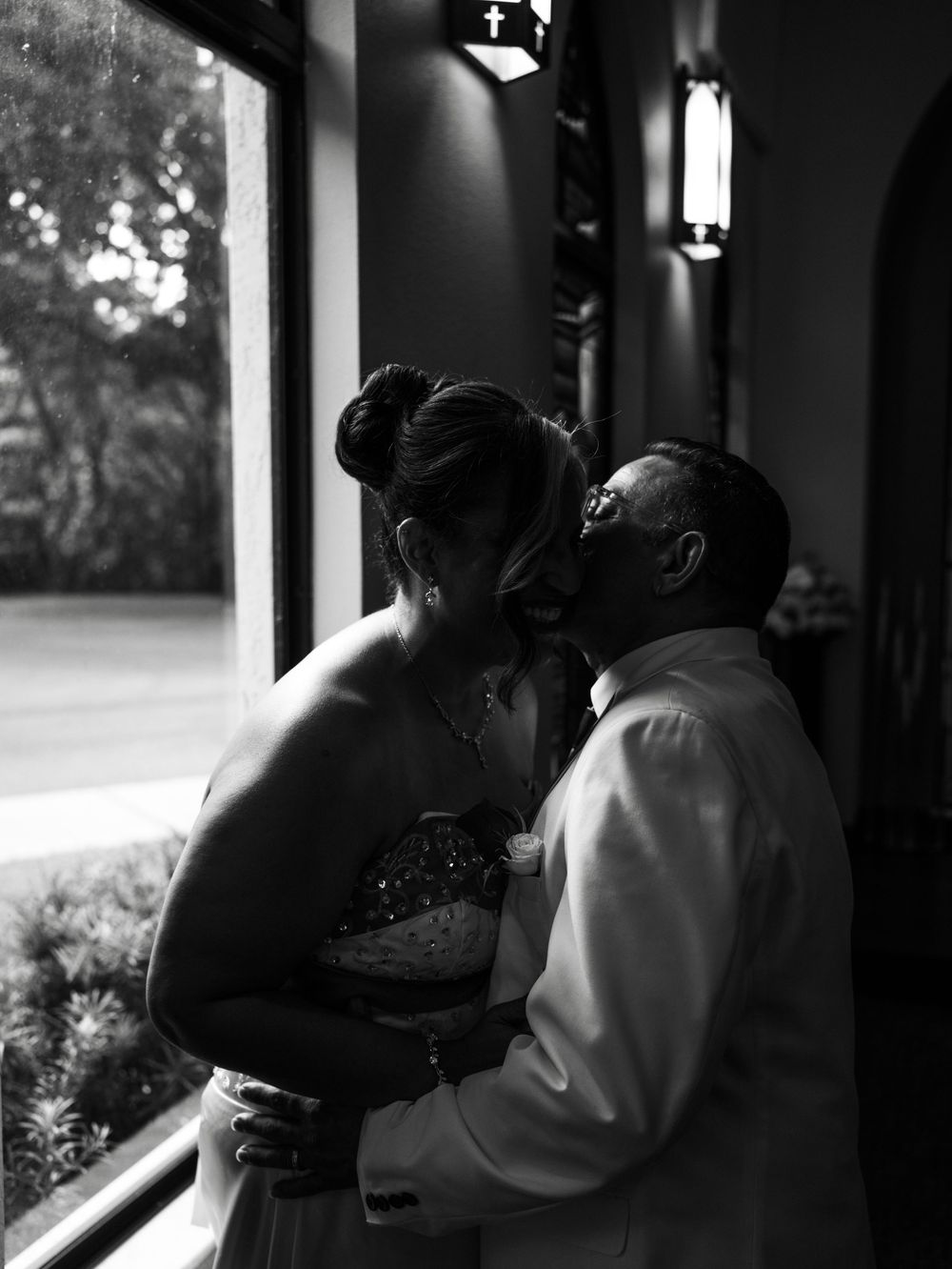 A romantic black and white photo series showing a couple sharing intimate moments in a window-lit space.