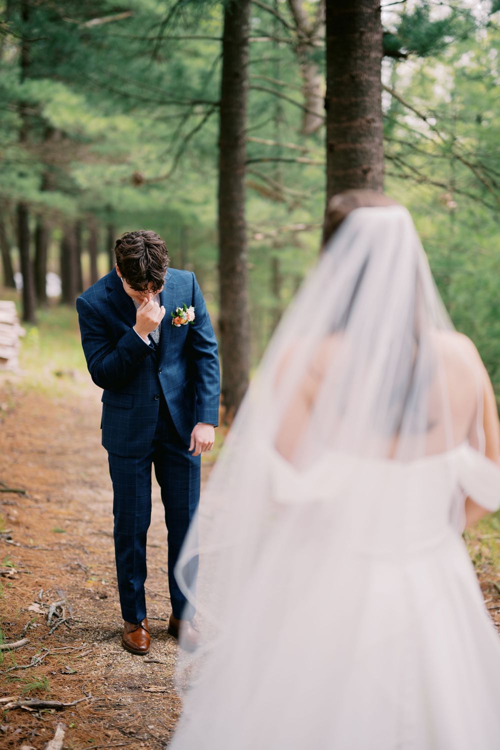 A romantic wedding photo sequence in a forest shows a couple sharing an emotional first look moment in blue suit and white gown.