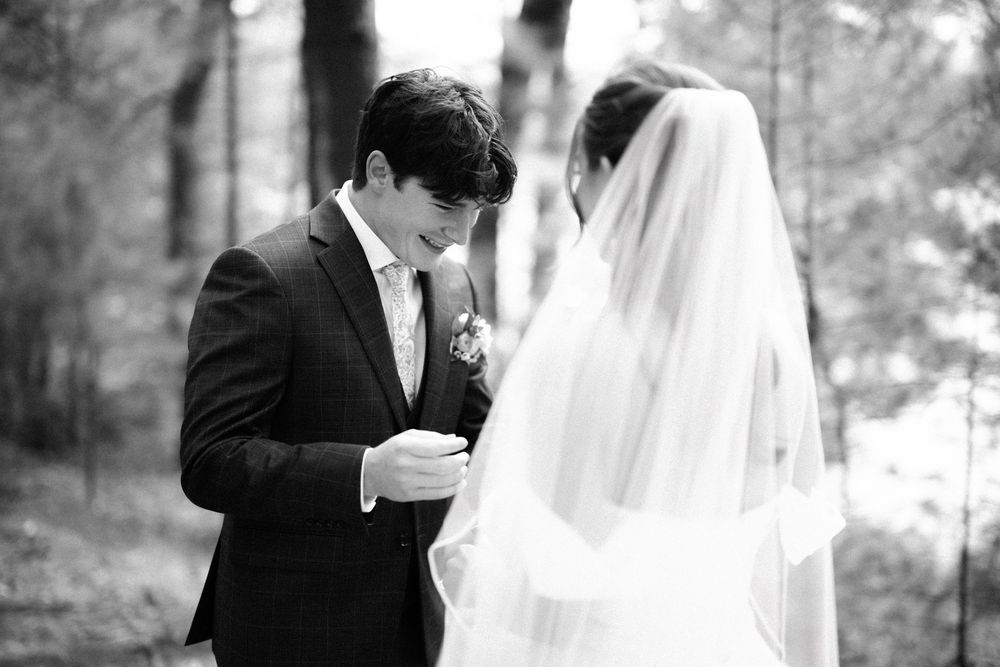 A black and white photo of a bride and groom during their wedding ceremony in a wooded outdoor setting.