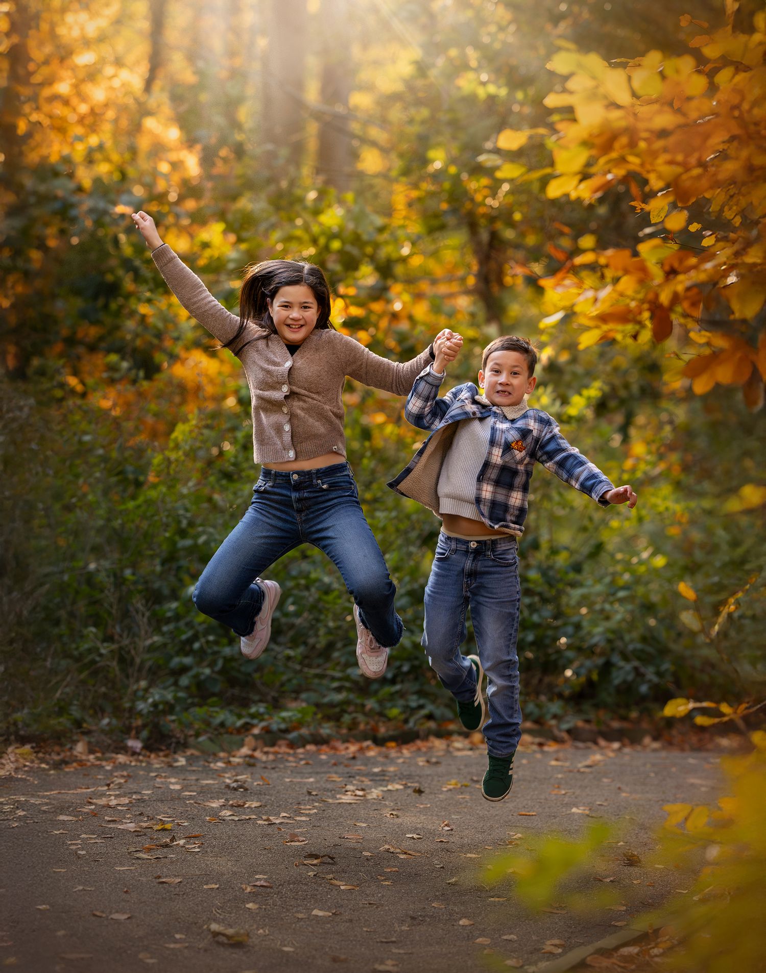 Kids jumping in Bramhall Park, surrounded by golden autumn leaves, and warm light and taken by Holly Dwyer, a family photograher in Cheshire