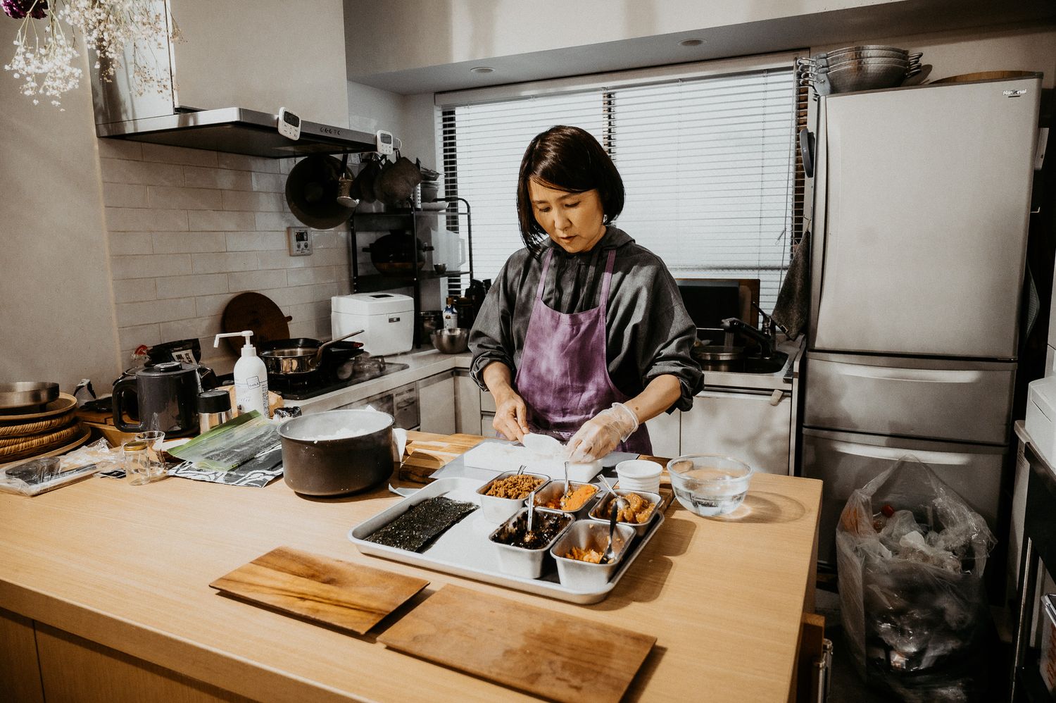 Woman cooking in a modern kitchen, preparing food on a wooden counter with various dishes and ingredients.