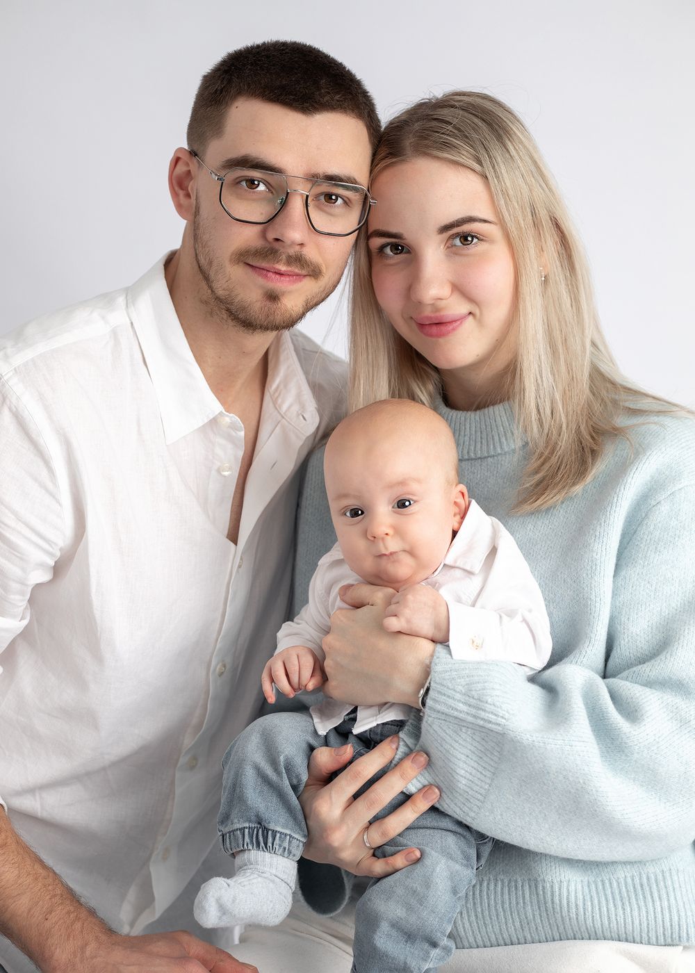 A series of family portraits showing parents in white and blue sweaters holding their baby against a light background.