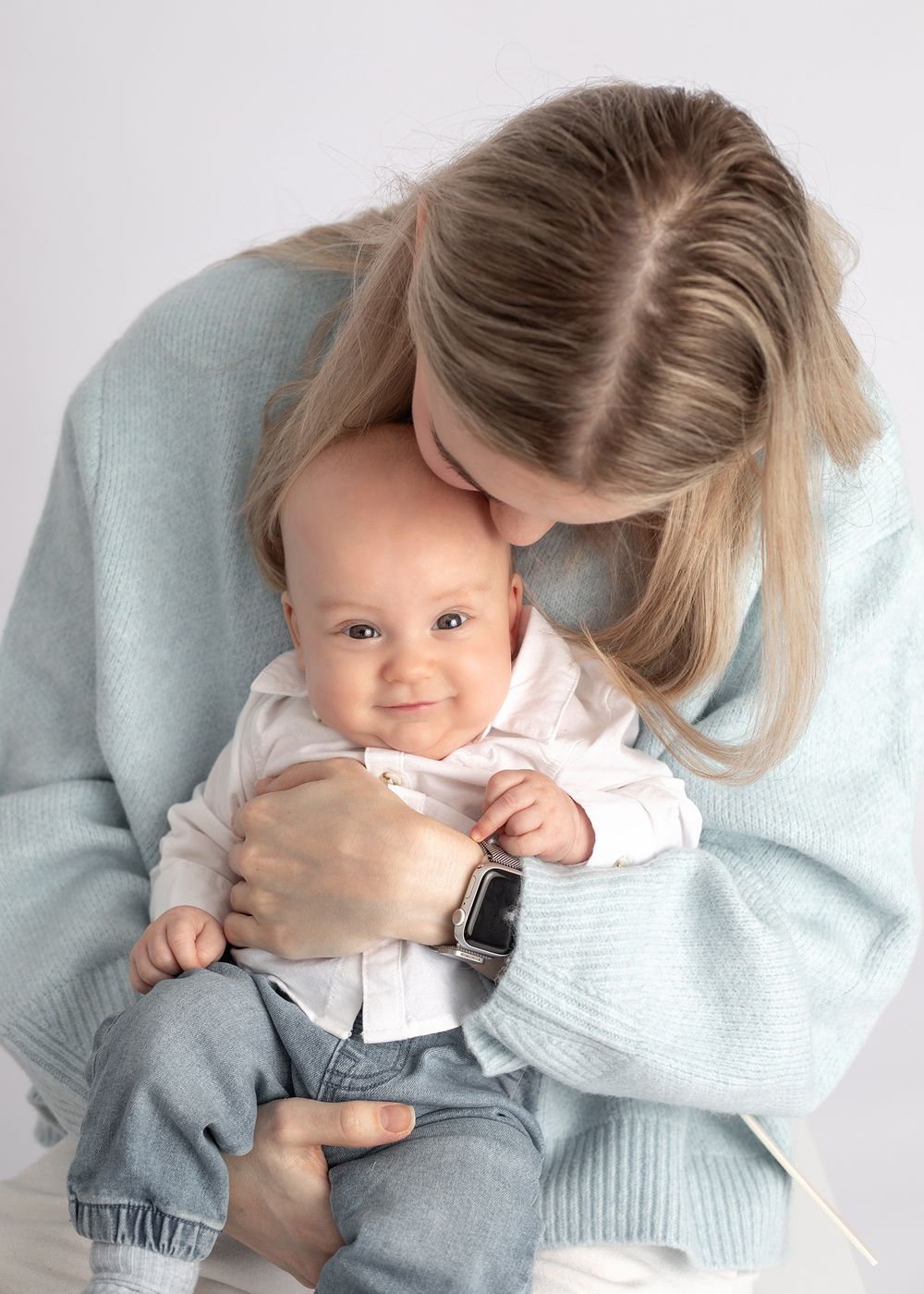 Sweet candid moments of parents cuddling and playing with their infant in matching light blue and white outfits.