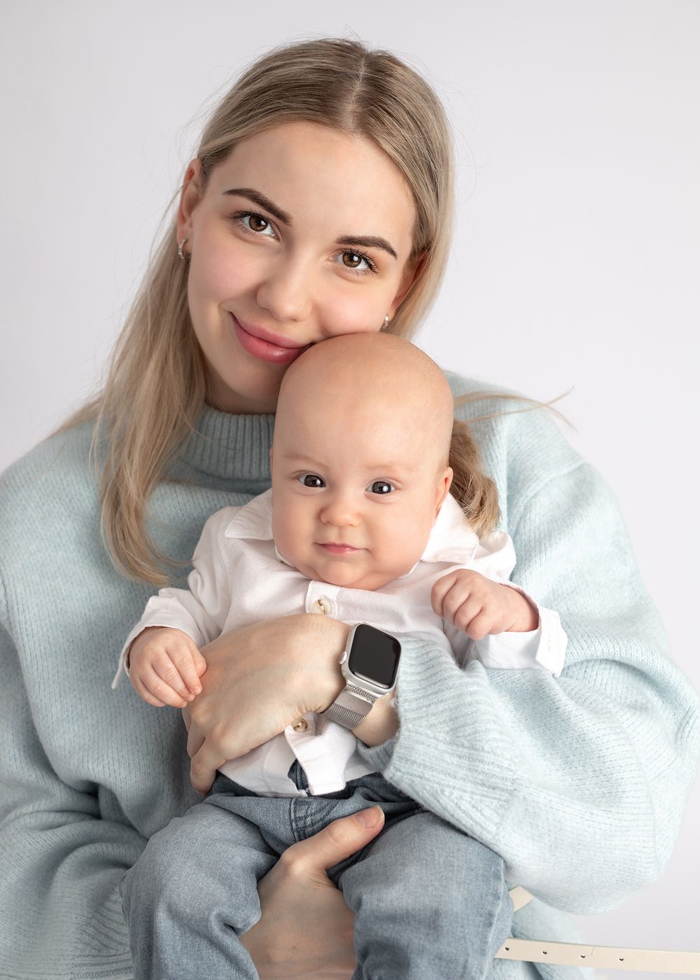 A parent in a light blue sweater shares tender moments with a baby wearing white and grey clothing.