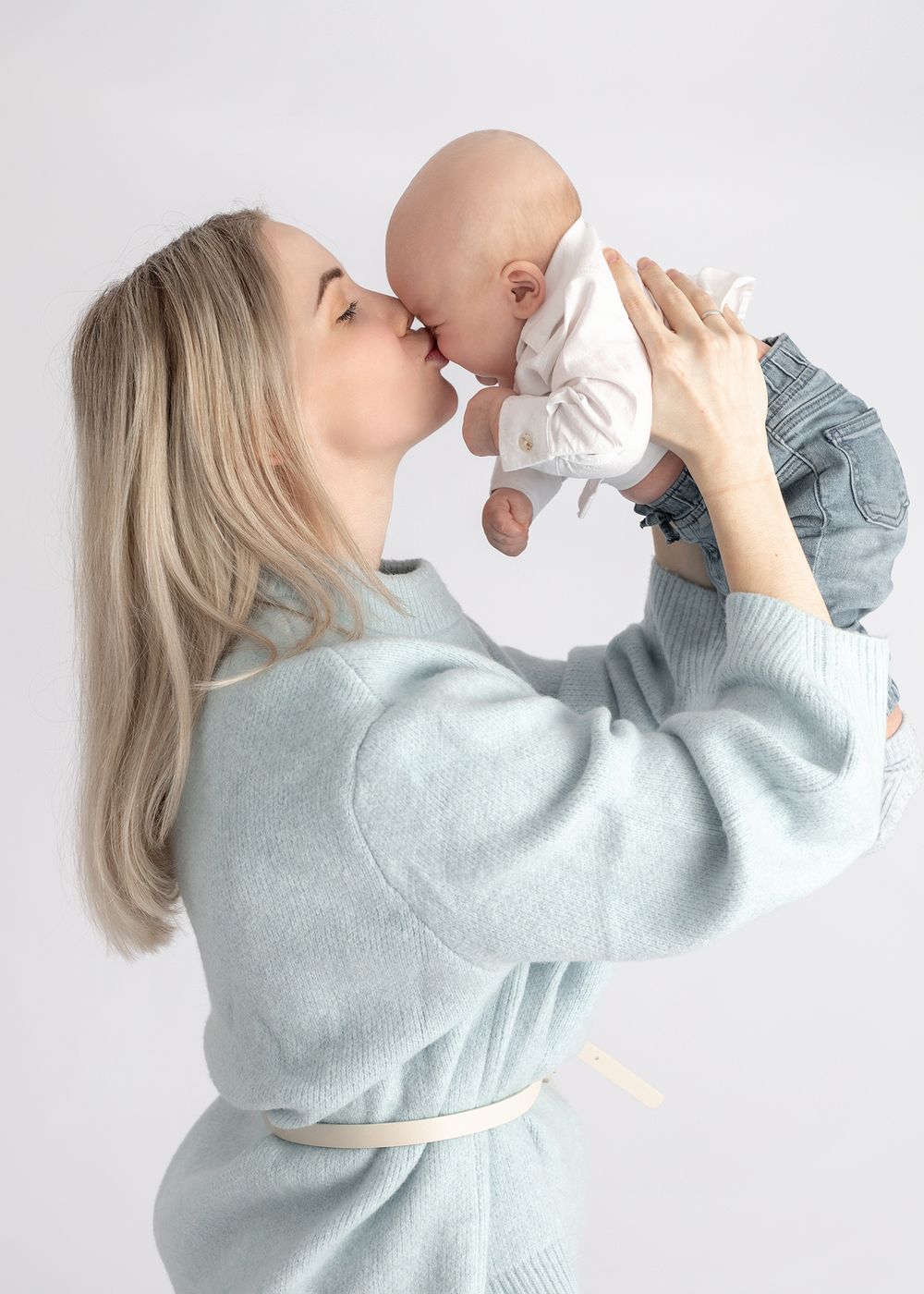A series of four photos showing someone in a light blue sweater lifting and playing with a baby against a white background.