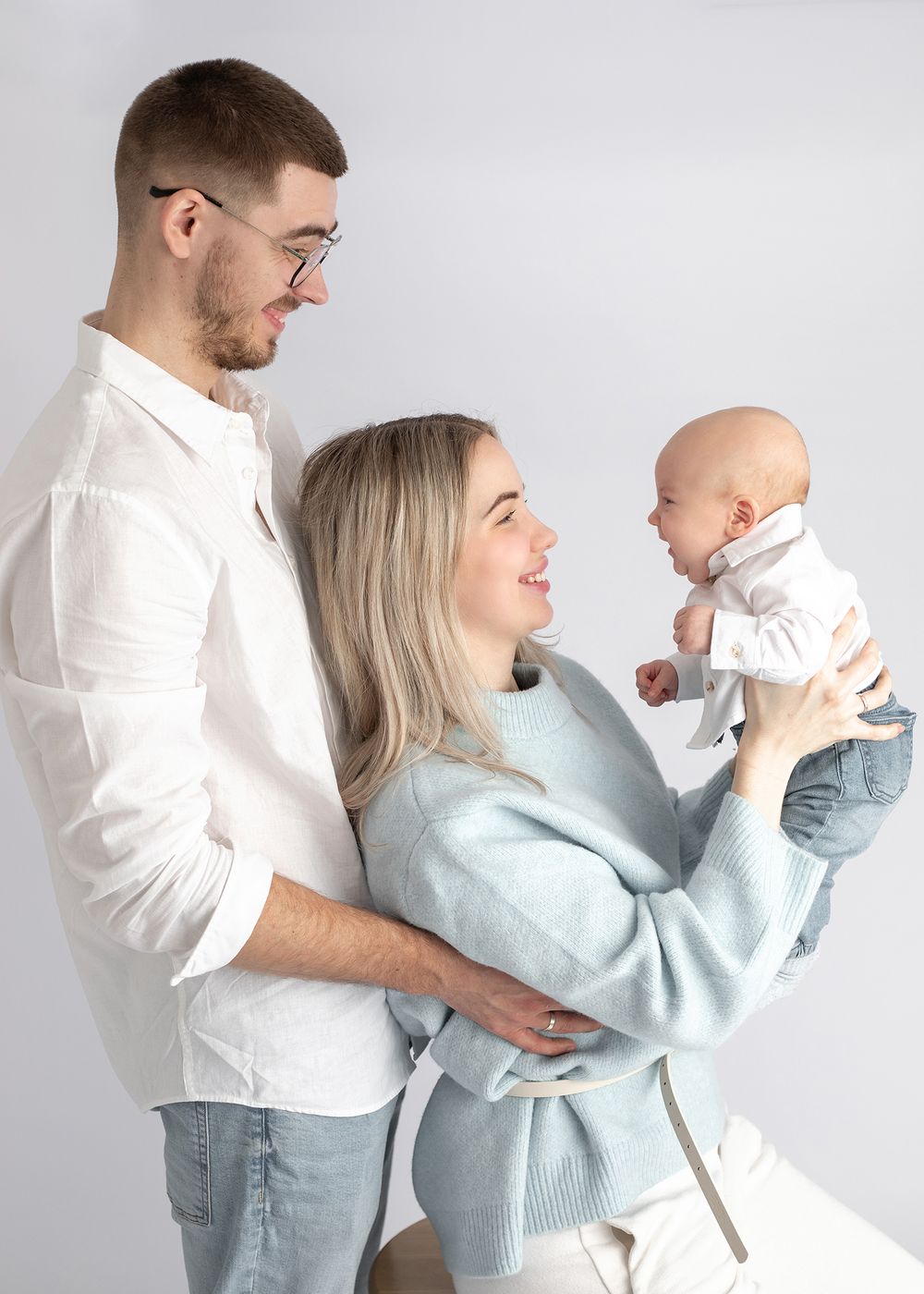 Happy family in matching white and light blue outfits share a tender moment against white background.