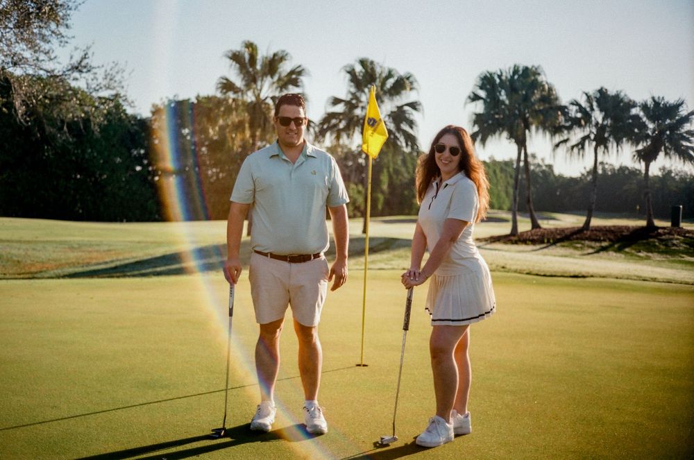 Golfers practicing putting on a sunny golf course with palm trees in the background at sunset.