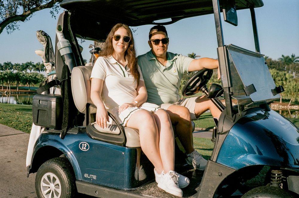 People enjoy a scenic ride in a golf cart along a sunny outdoor path during a warm day.