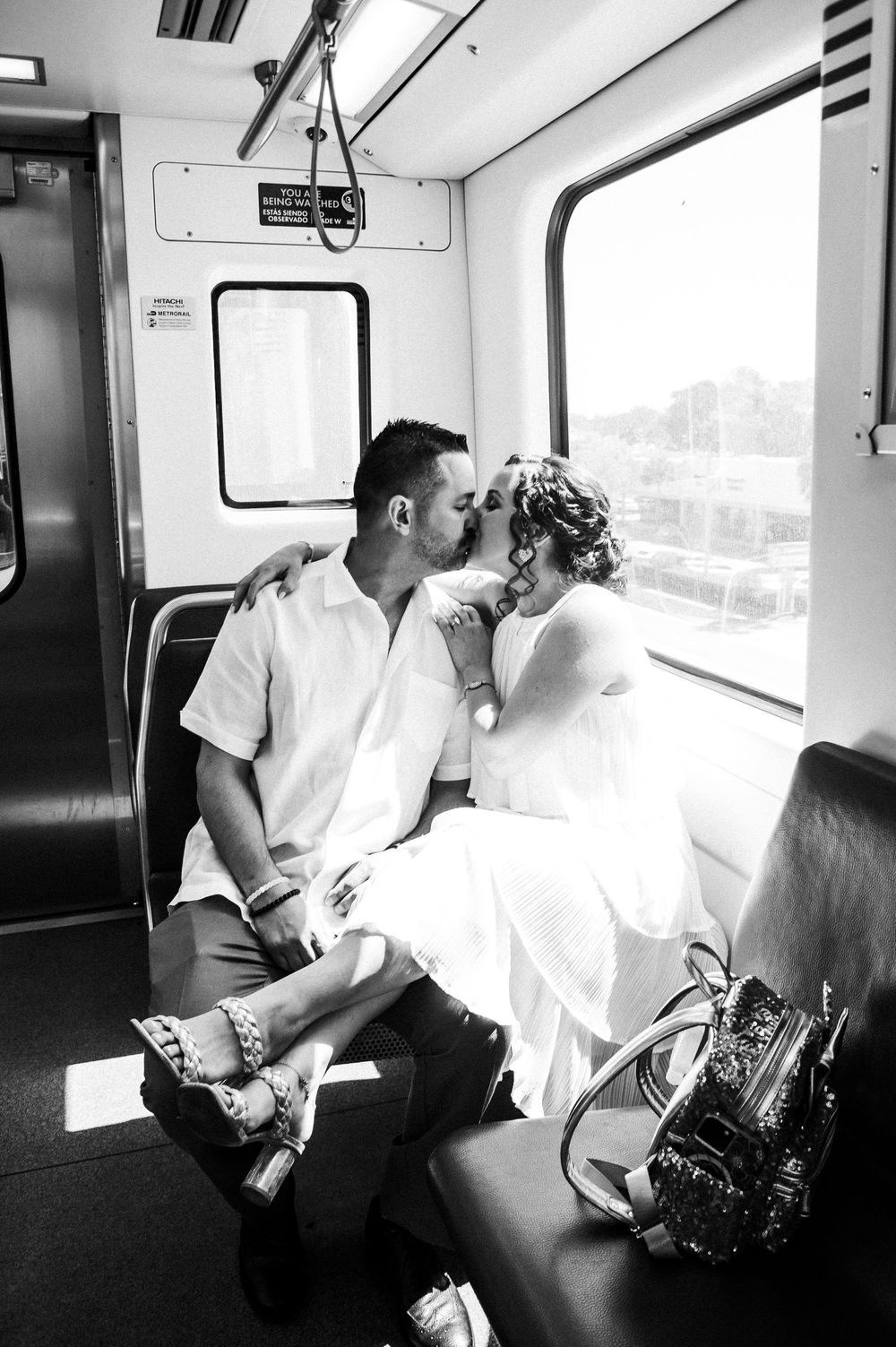 Two people share a tender moment while riding on public transit in black and white photography.