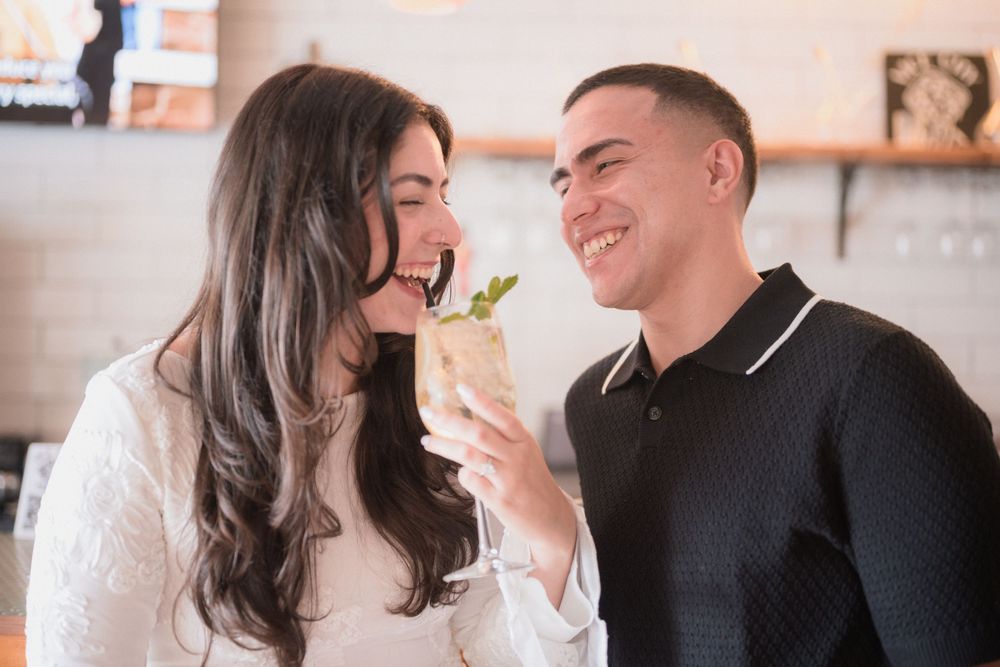 A smiling couple shares a cocktail garnished with mint at a modern restaurant bar.