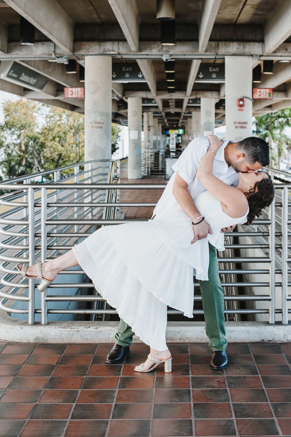 A romantic dip pose under an urban overpass with tiled flooring and concrete columns.