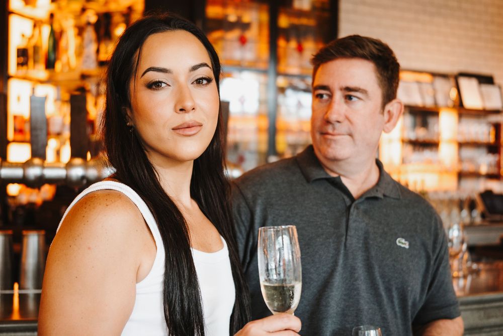 People enjoying drinks and conversation at a warmly lit bar with modern decor and exposed brick walls.