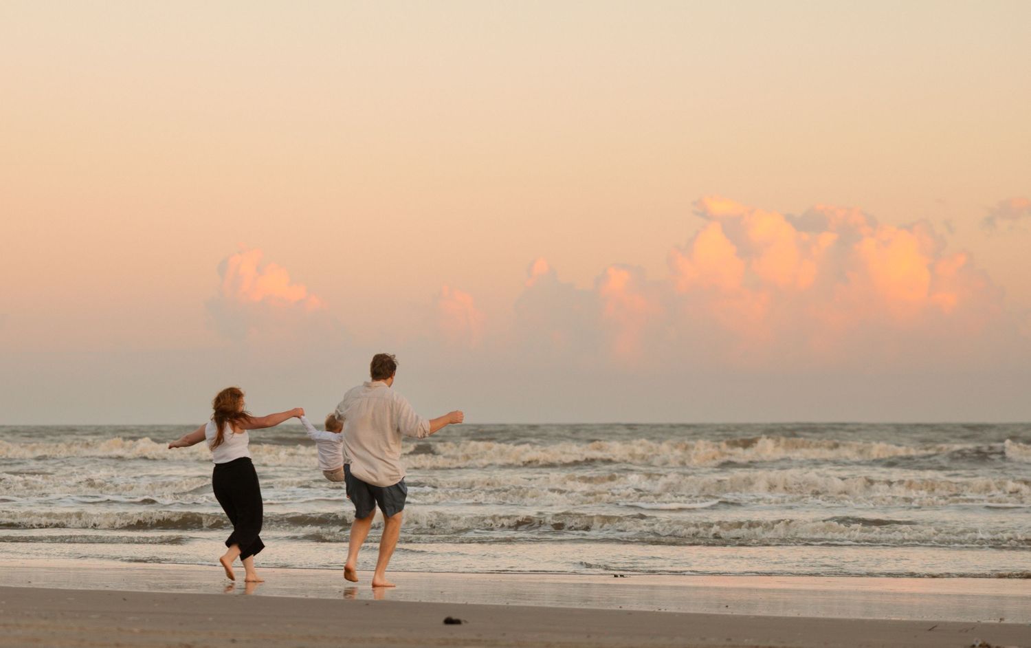 A romantic sunset beach photoshoot with silhouettes walking along the shoreline at dusk.
