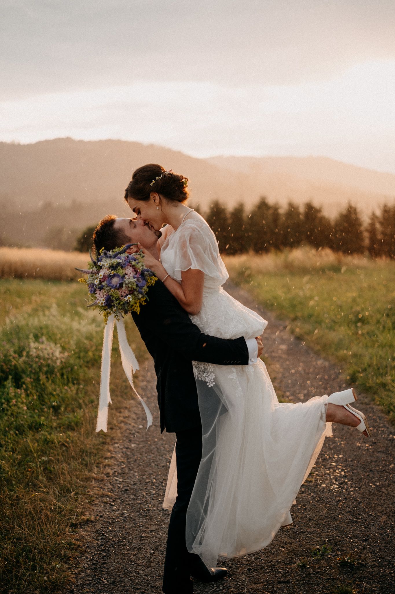 Romantic sunset wedding photo series showing couple embracing on a mountain trail with wildflowers and golden light.
