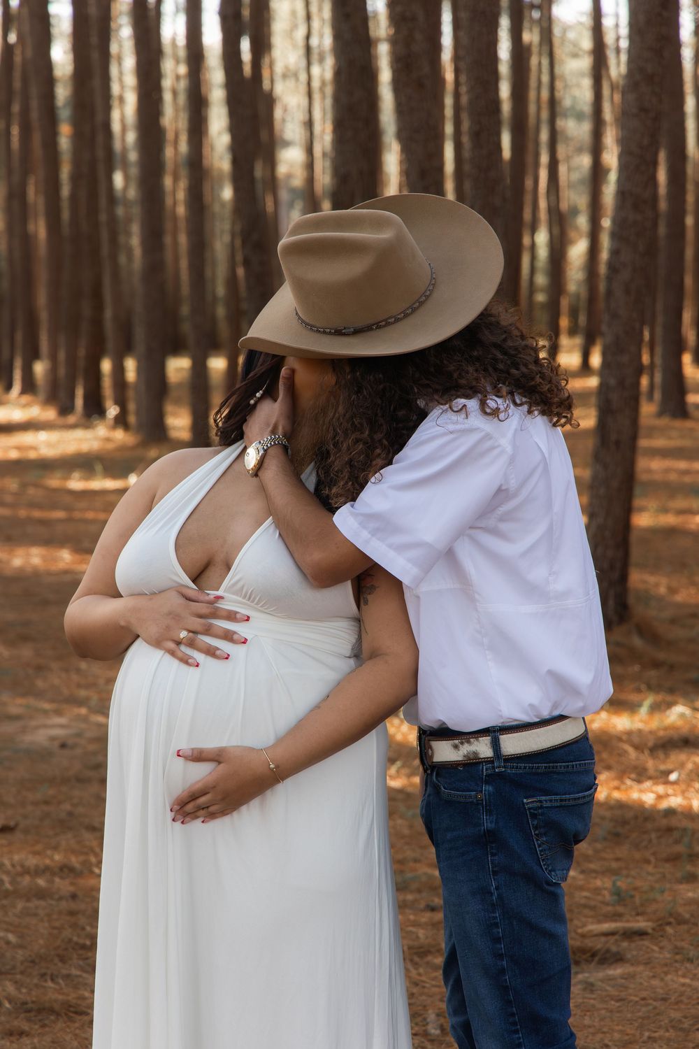 Romantic maternity photo series showing couple embracing in a sunlit forest setting.
