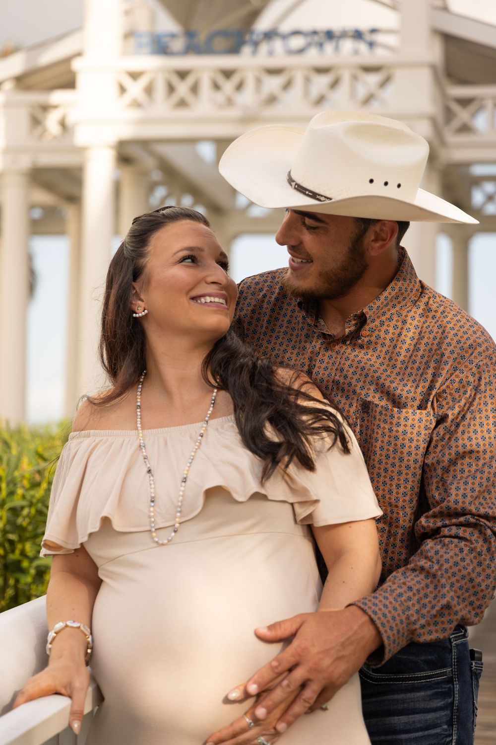 A couple shares intimate moments in a series of maternity photos wearing western attire against an elegant architectural backdrop.