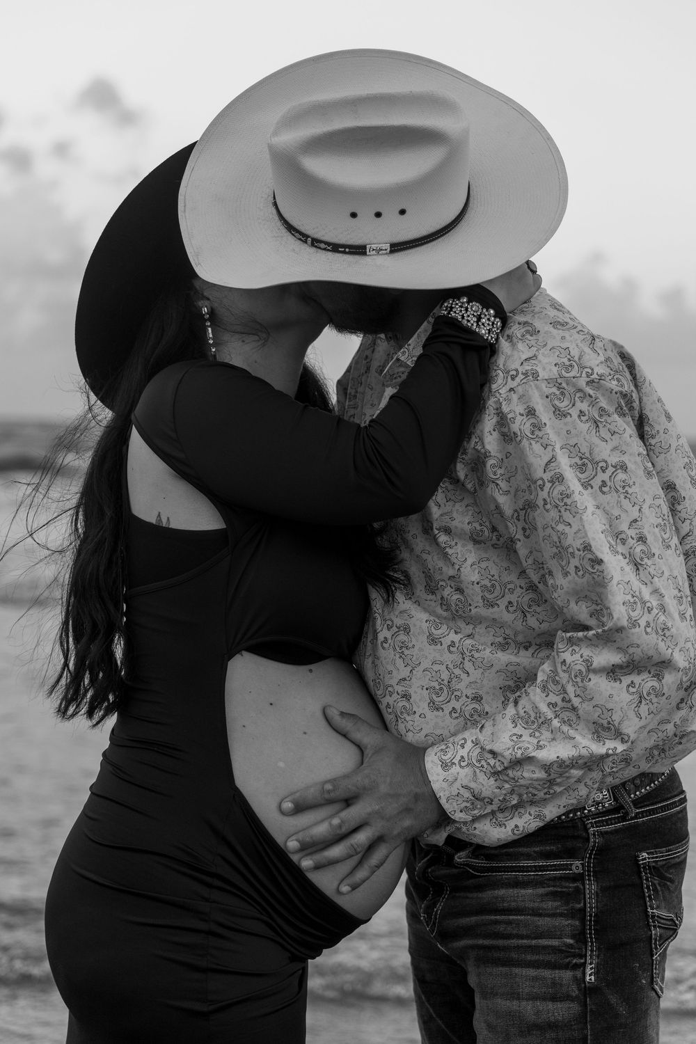 A black and white photo series showing a couple in western wear embracing in romantic poses against a rustic backdrop.