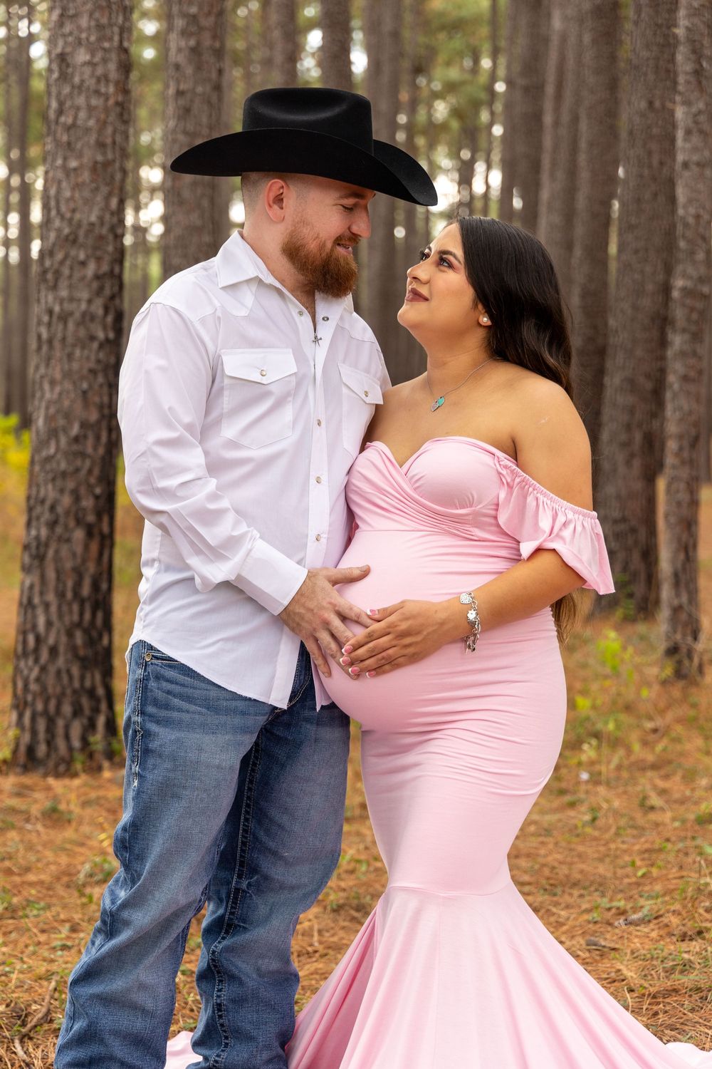 A romantic couple in pink dress and white shirt dance together in a forest setting.